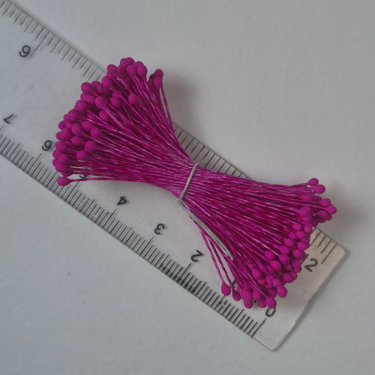 A bundle of size L Japanese miniature flower stamens, featuring vibrant fuchsia heads on matching fuchsia cotton threads, arranged next to a transparent ruler