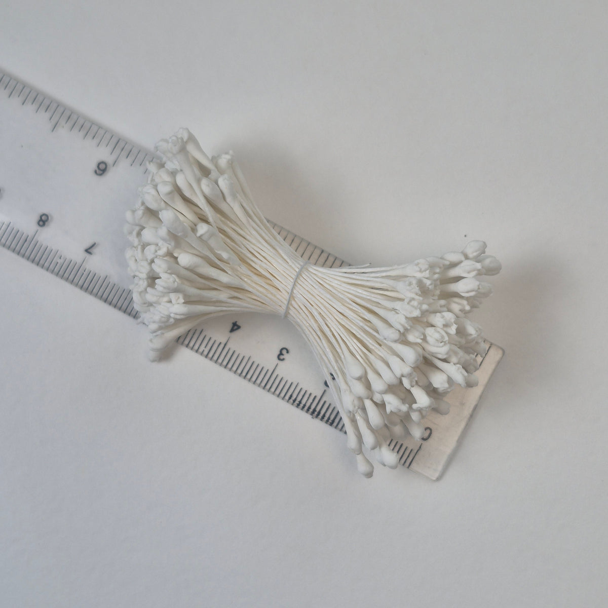 A bundle of extra-large size XL naturalistic Japanese flower stamens made of white rice flour and rayon threads, arranged next to a transparent ruler
