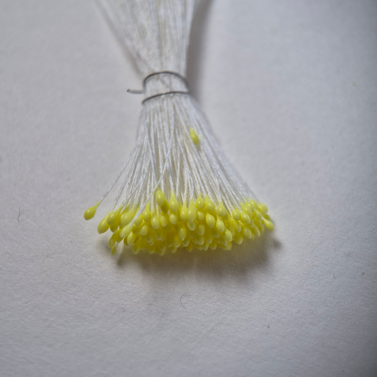 Small bundle of tiny yellow round flower stamens on snow white cotton thread for silk floristry
