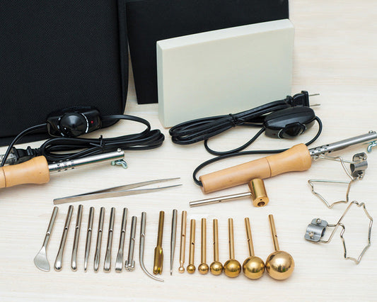 Collection of metal tools and accessories for fabric flowers making on a white surface with a black background.
