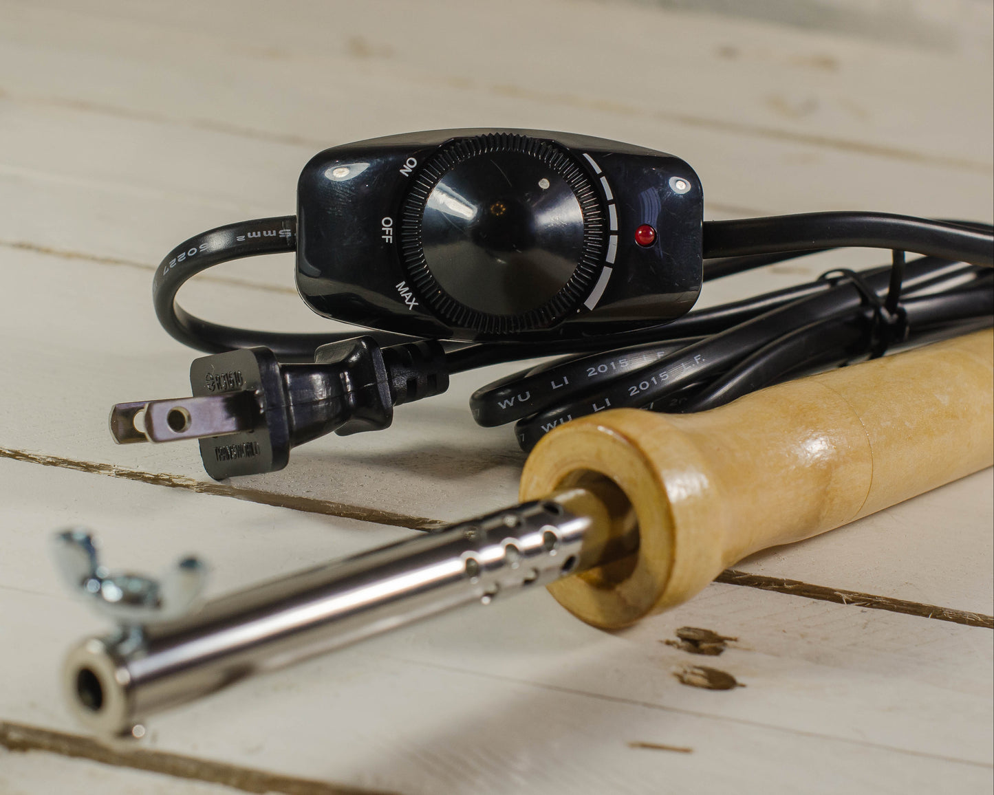Wooden-handled soldering iron with control knobs on a wooden surface