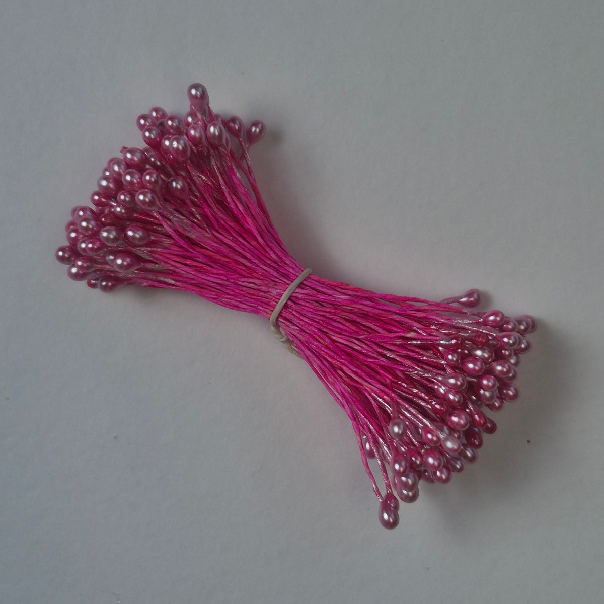 A bundle of size L Japanese miniature flower stamens, featuring bright pink pearlescent heads on vibrant raspberry cotton threads, arranged next to a transparent ruler