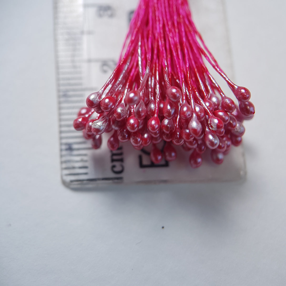 A bundle of size L Japanese miniature flower stamens, featuring bright pink pearlescent heads on vibrant raspberry cotton threads, arranged next to a transparent ruler
