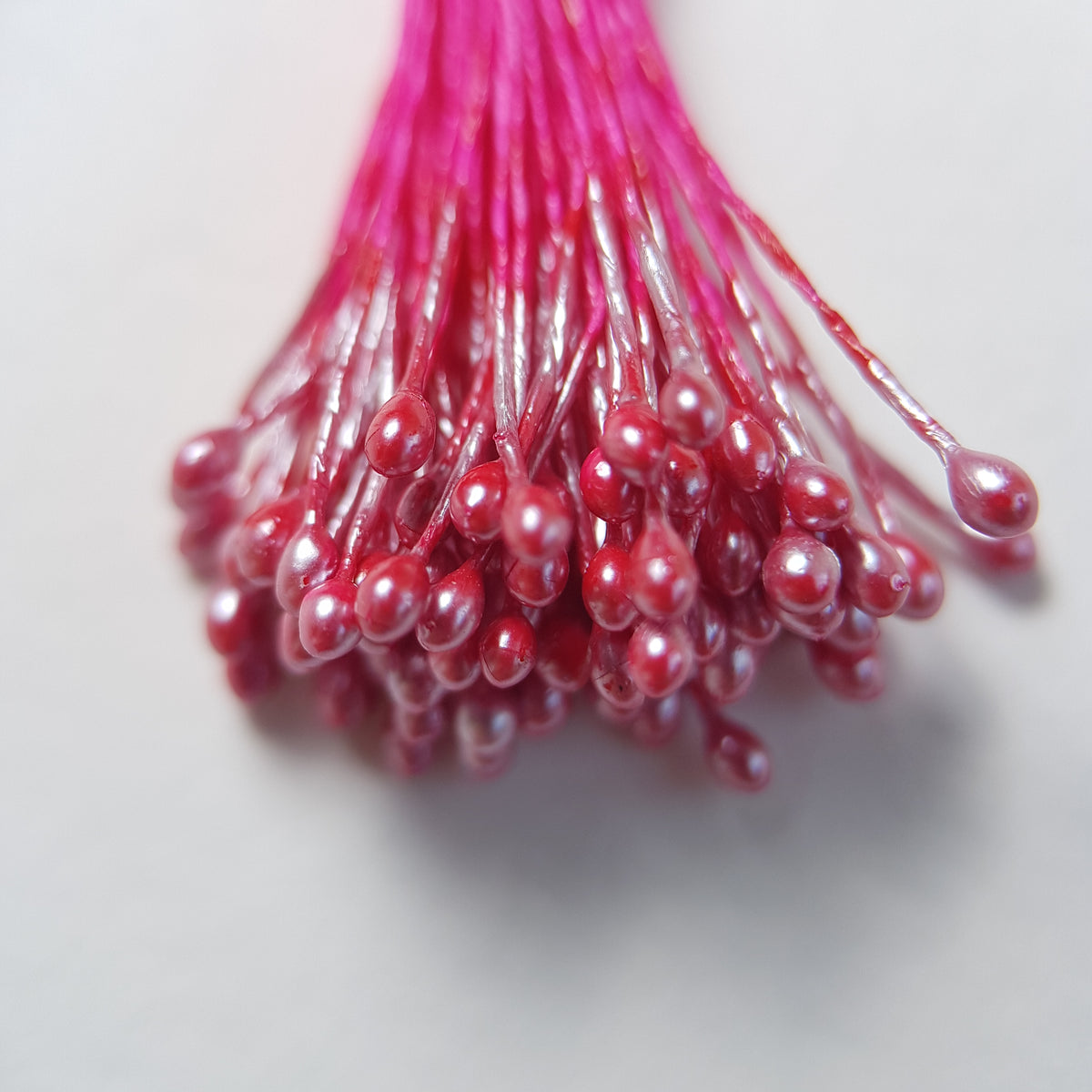A bundle of size L Japanese miniature flower stamens, featuring bright pink pearlescent heads on vibrant raspberry cotton threads, arranged next to a transparent ruler