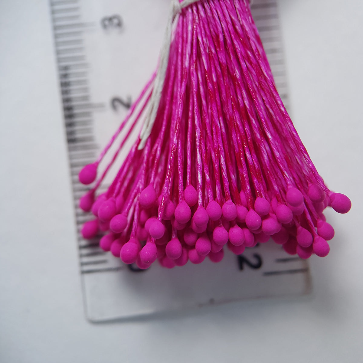 A bundle of size L Japanese miniature flower stamens, featuring vibrant fuchsia heads on matching fuchsia cotton threads, arranged next to a transparent ruler