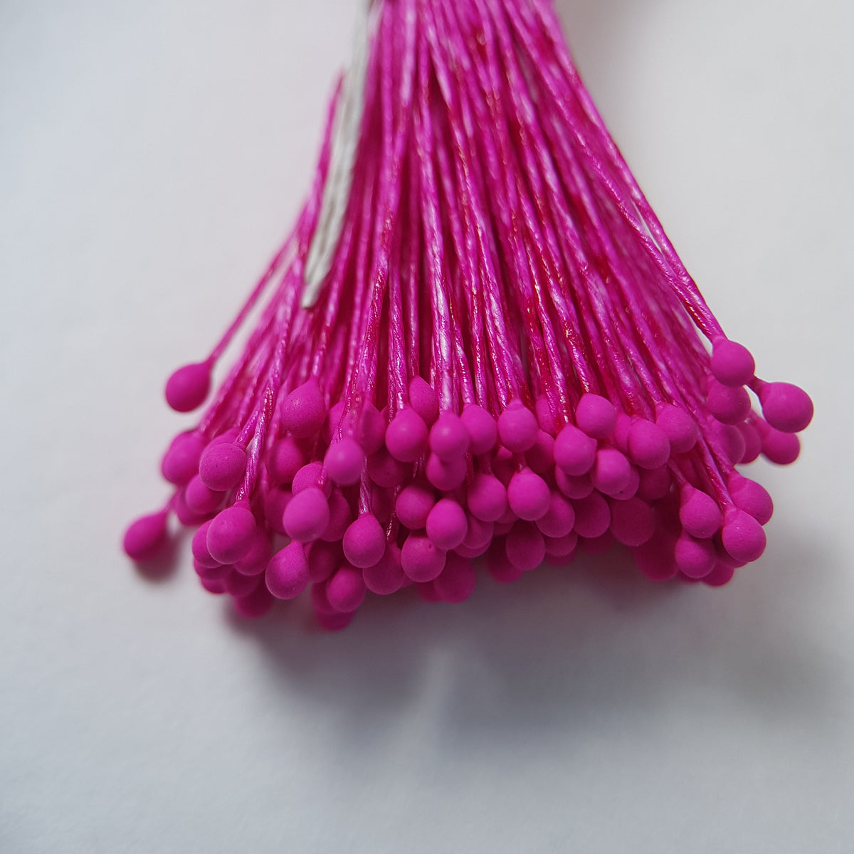 A bundle of size L Japanese miniature flower stamens, featuring vibrant fuchsia heads on matching fuchsia cotton threads, arranged next to a transparent ruler