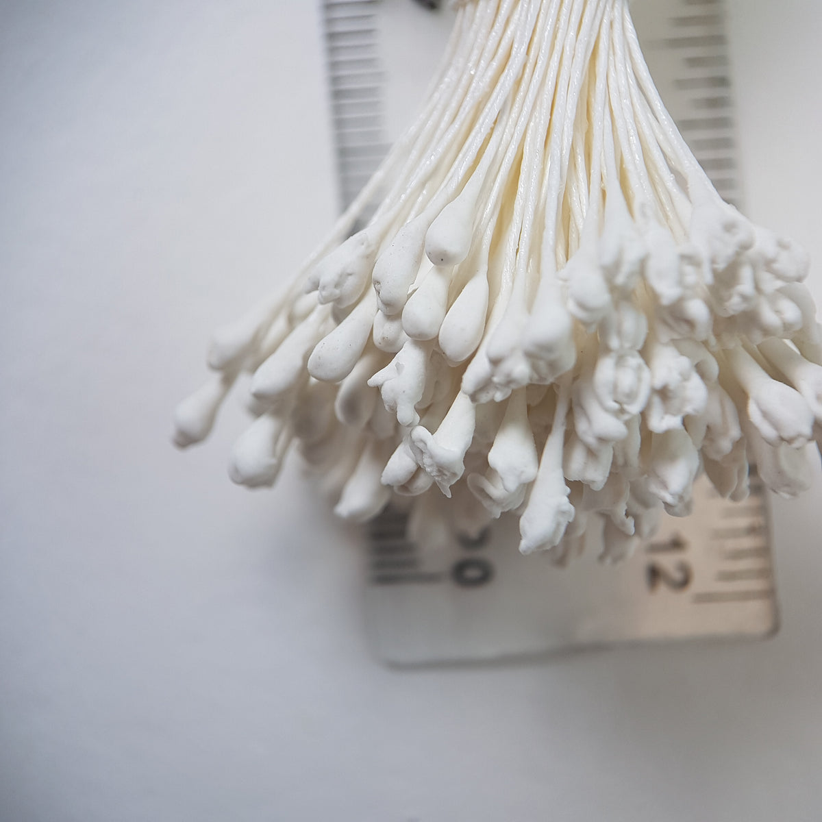A bundle of extra-large size XL naturalistic Japanese flower stamens made of white rice flour and rayon threads, arranged next to a transparent ruler