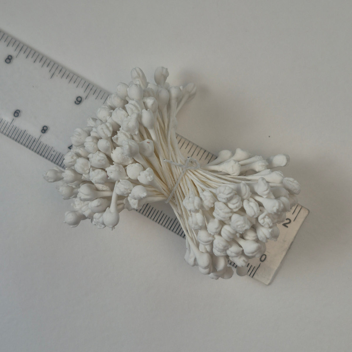 A bundle of extra-large size XL naturalistic Japanese flower stamens made of white rice flour and rayon threads, arranged next to a transparent ruler
